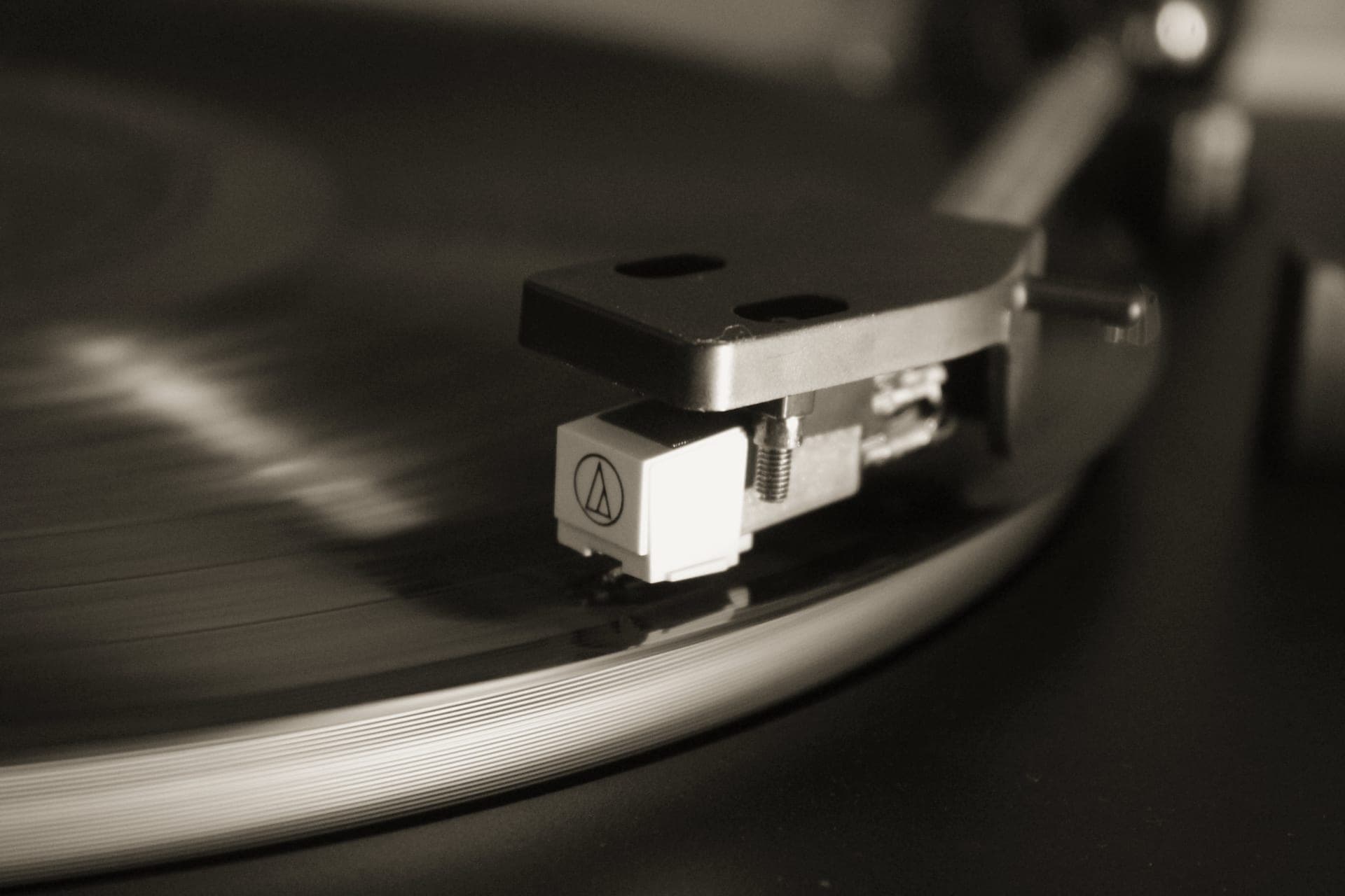 A turntable tonearm and stylus tracking a record groove under warm low-key light